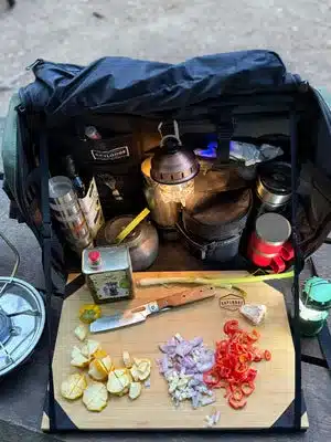 Workspace Mobile Camp Kitchen mit Bambustisch, Küchenutensilien und geschnittenem Gemüse beim Outdoor-Einsatz.