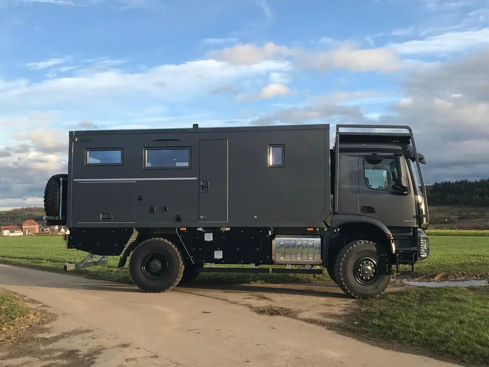 Schwarzes Mercedes-Benz Arocs 4x4 Expeditionsmobil mit Woelcke GFK-Wohnaufbau auf einer ländlichen Straße