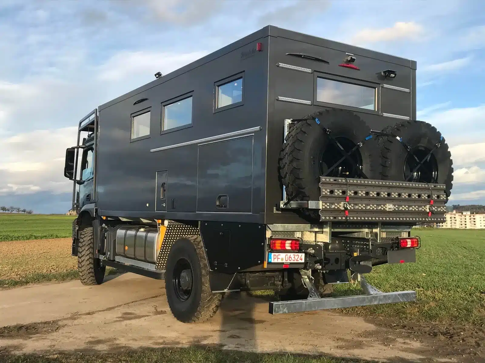 Schwarzes Mercedes-Benz Arocs 4x4 Expeditionsmobil mit Woelcke Wohnaufbau auf einem Feldweg