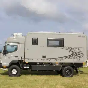 Seitliche Ansicht des Autark Explorer WOE 2017 Expeditionsmobils auf Fuso Canter 4x4 auf einer Wiese unter bewölktem Himmel.