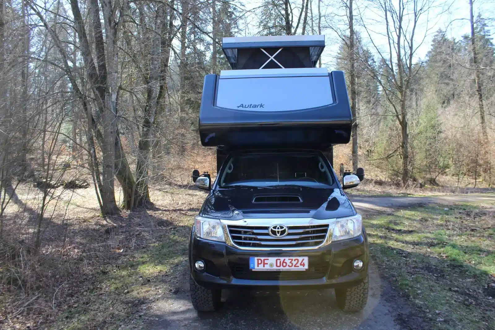 Schwarzer Autark Hilux Extra Cab 2018 mit aufgeklapptem Hubdach auf einem Waldweg
