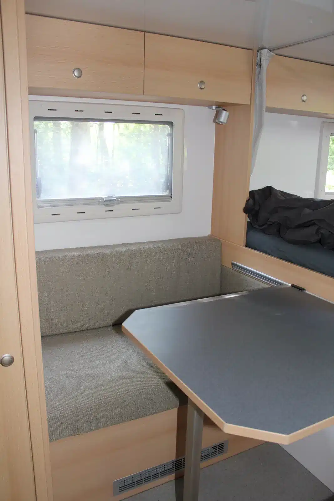 Sitzgruppe mit grauem Polster, Tisch und Fenster im Innenraum eines Woelcke Autark Hilux Offroad-Campers