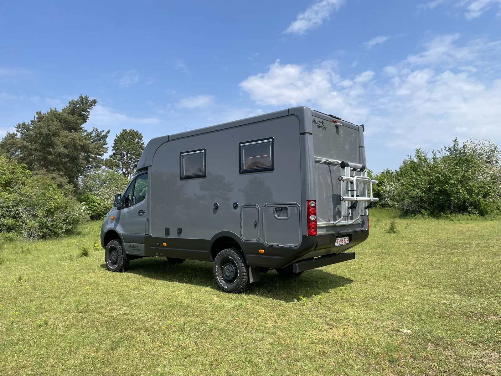 Allradwohnmobil Autark Runner R9 – 2023, seitliche Ansicht auf einer Lichtung, mit Fahrradträger und großen Fenstern