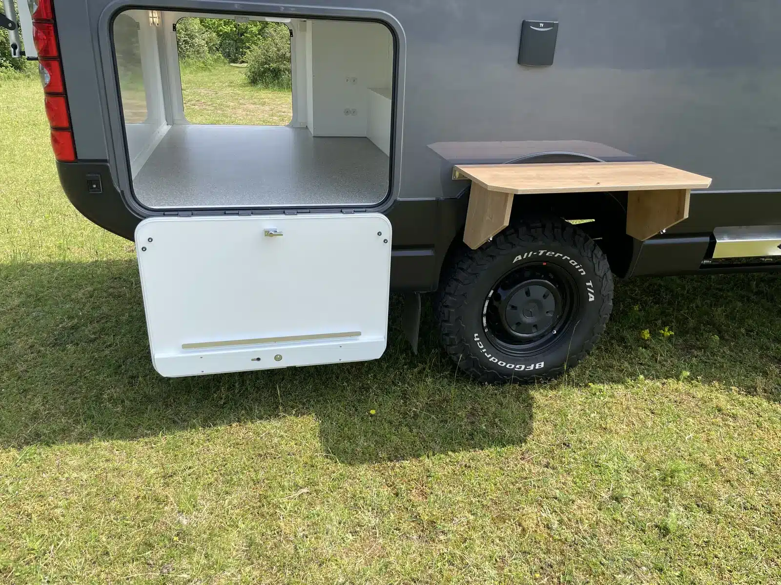 Heckstauraum mit geöffneter Klappe und ausgeklapptem Tisch am Autark Runner R9 auf einer Wiese