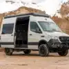 VANME BEDROCK 4x4-Campervan auf Sprinter-Basis mit geöffnetem Schiebetür, Offroad-Umbau und Dachaufbau auf schlammigem Untergrund