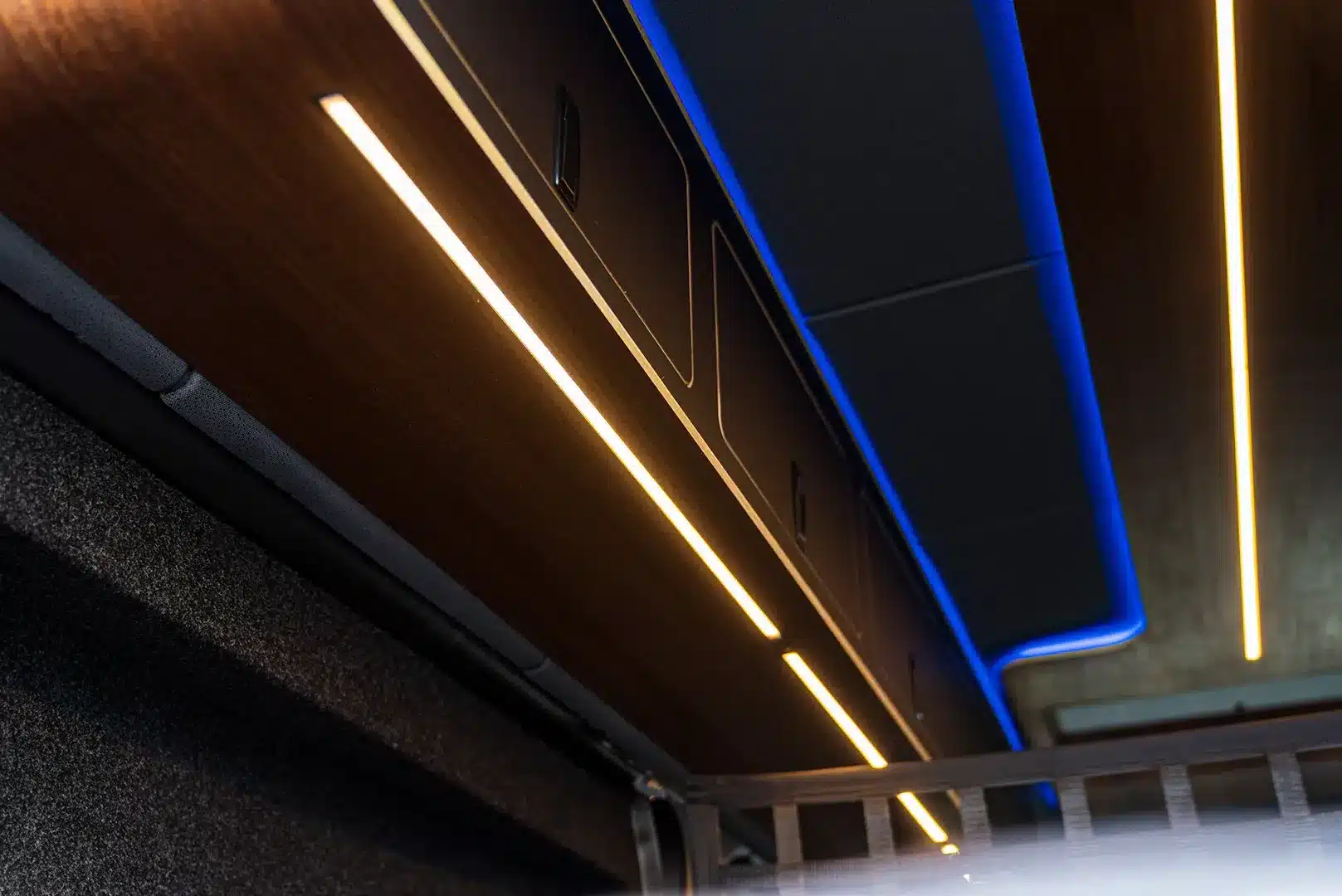 LED-Lichtbänder und dunkle Holzoberschränke im Innenraum des VANME BEDROCK Reisemobils