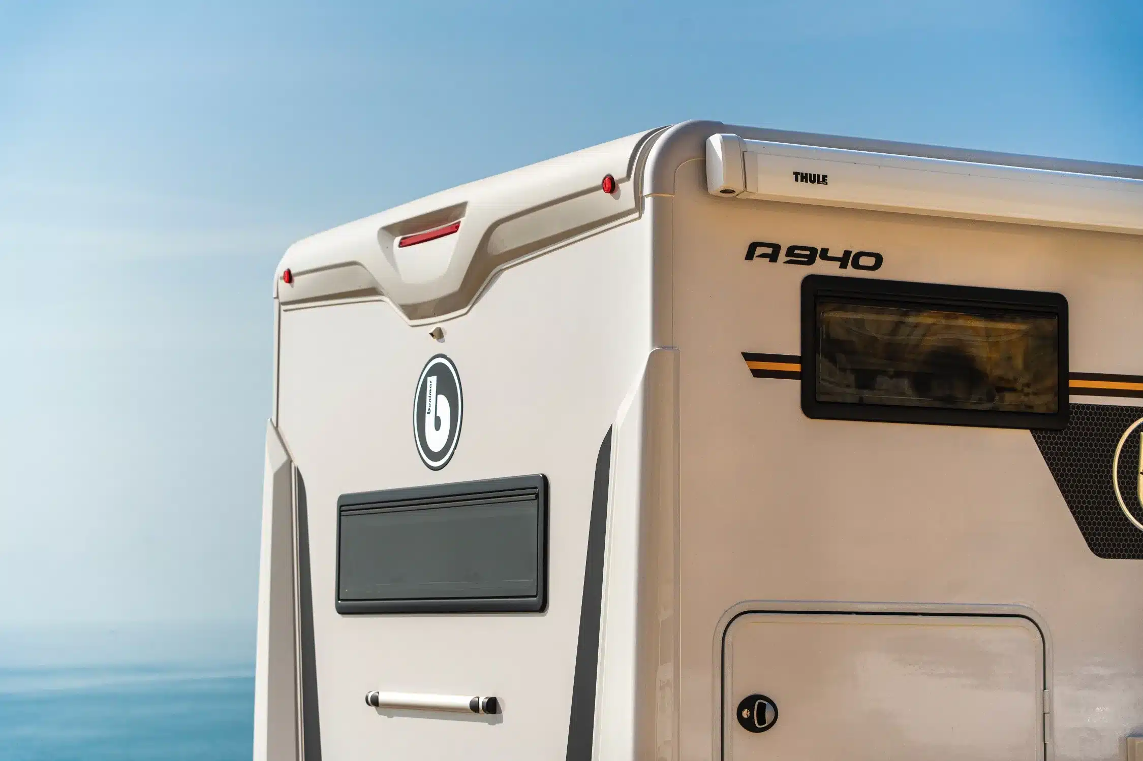 Heckpartie des Benimar Amphitryon A940 Reisemobils mit Logo, Fenster und Garage vor blauem Himmel.