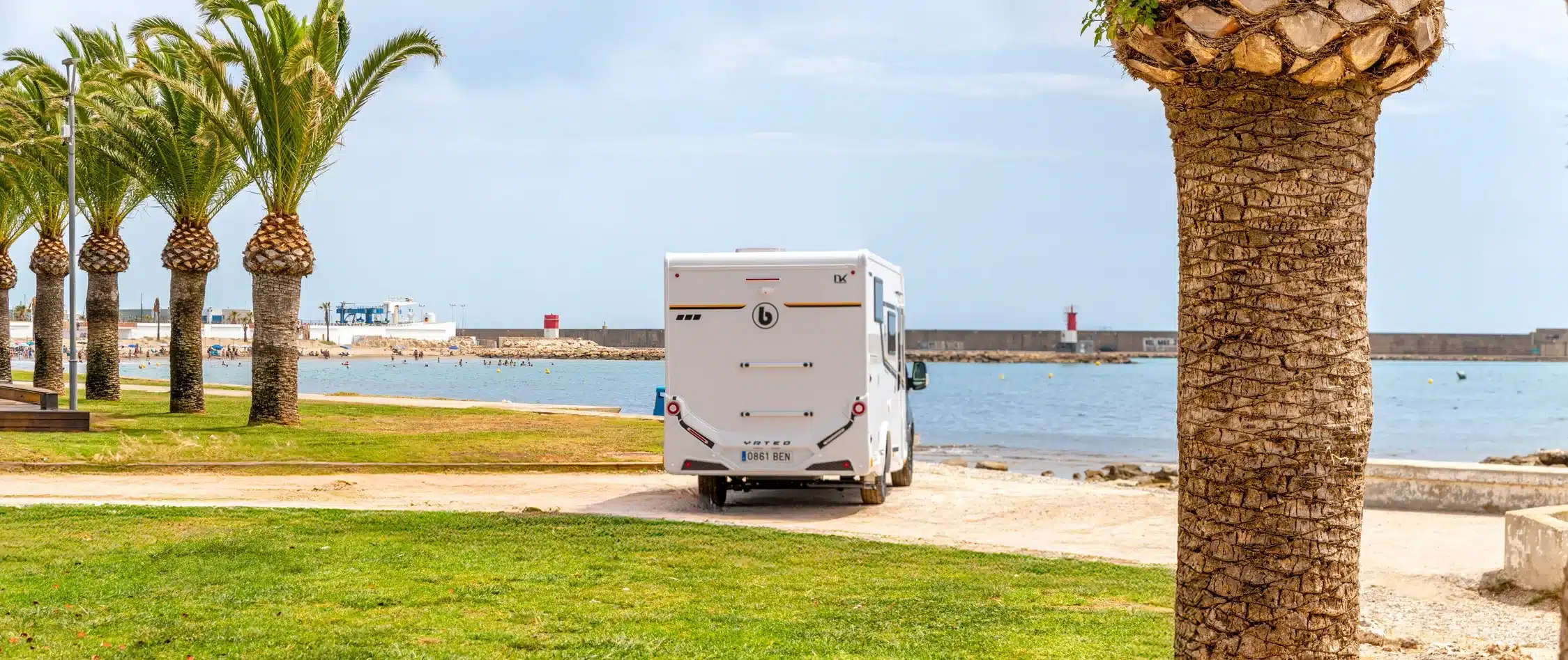 Heckansicht eines Benimar Y861 Wohnmobils am Meer, umgeben von Palmen.