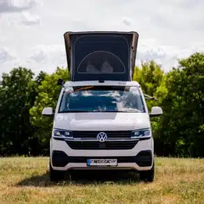 VW T6.1 BIWAK Camper mit geöffnetem Aufstelldach, stehend auf einer grünen Wiese vor Bäumen