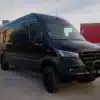 Schwarzer Black Gorilla Campervan auf Mercedes-Benz Sprinter 4x4 vor Containern.
