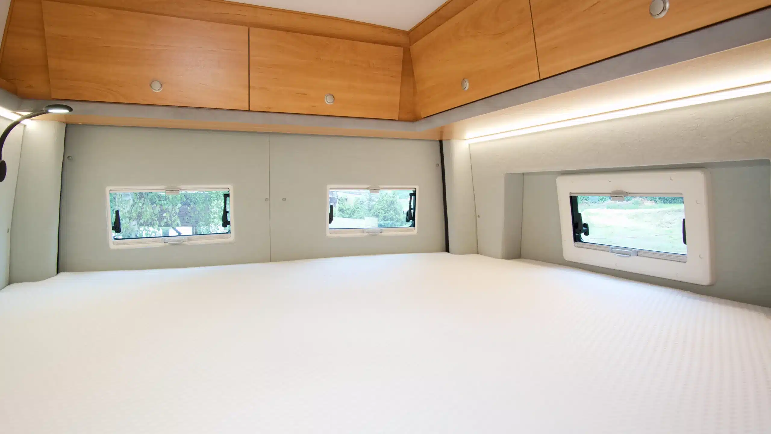 Blick auf das große Heckquerbett mit drei Fenstern und Oberschränken im Kastenwagen Bresler 694 DF