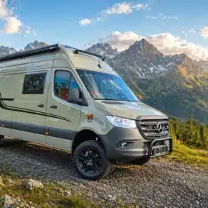 Bresler 694 DG – Indi Cross Campervan in einer alpinen Landschaft auf einem Schotterweg, umgeben von Bergen und Wald.