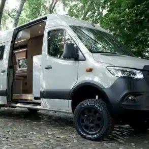 Bunnylounge 2.0 Familiencamper Mercedes-Benz Sprinter mit geöffneter Schiebetür auf einem Waldparkplatz.