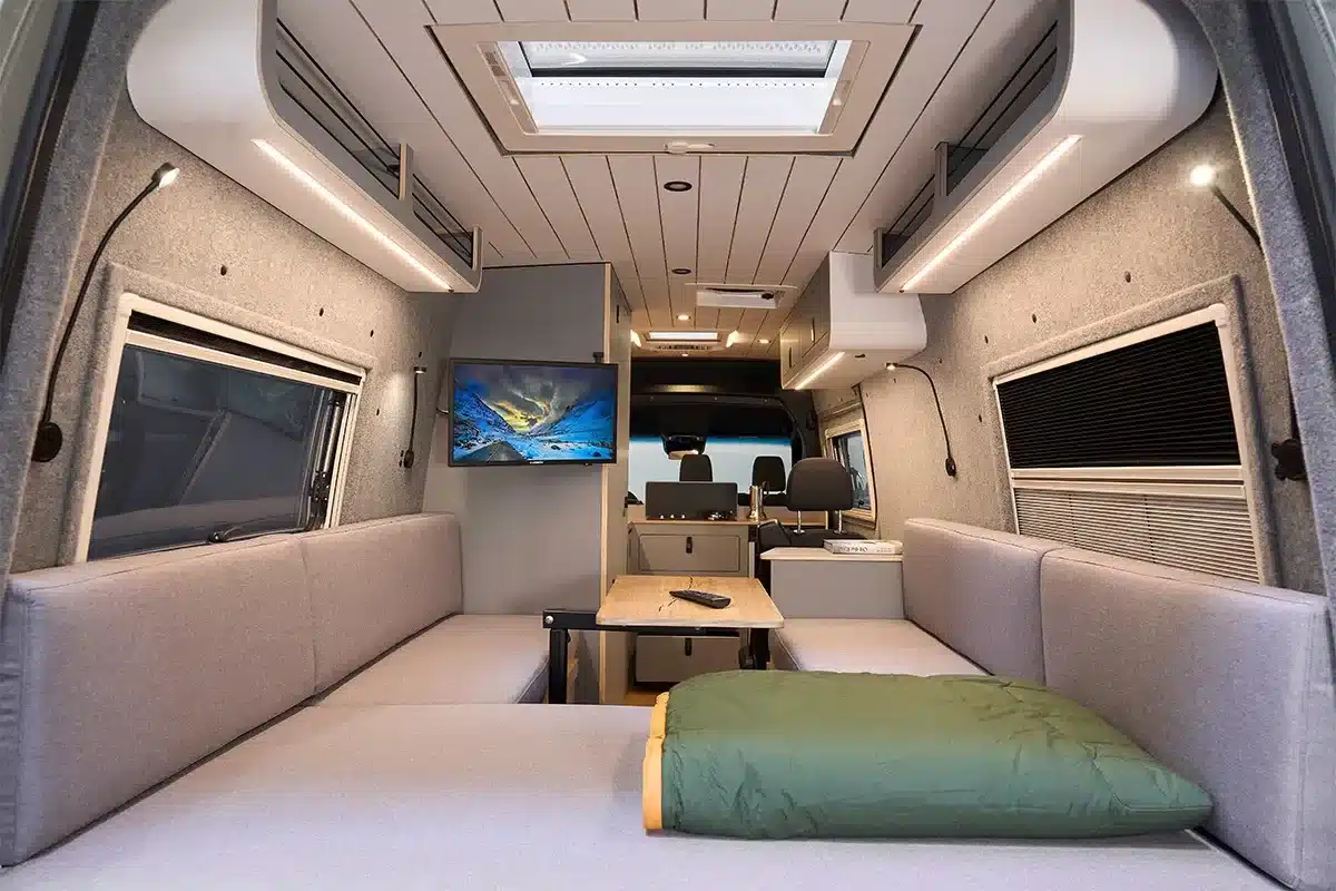 Innenansicht des Bunnylounge 2.0 mit u-förmiger Sitzecke, Tisch und TV im Camper.
