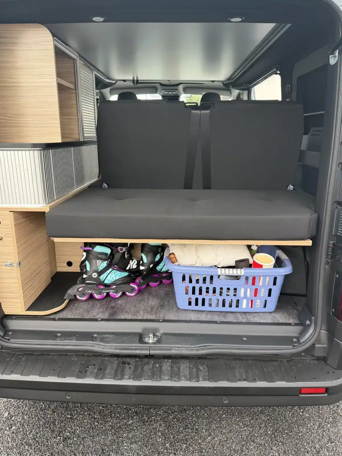Blick in den geöffneten Kofferraum eines Mooveo Campervan 2 mit Sitzbank, Stauraum, Rollschuhen und Wäschekorb