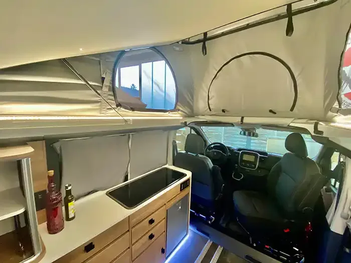 Blick in den Innenraum des Mooveo CAMPERVAN 3 mit geöffnetem Aufstelldach, Küchenzeile und Cockpit