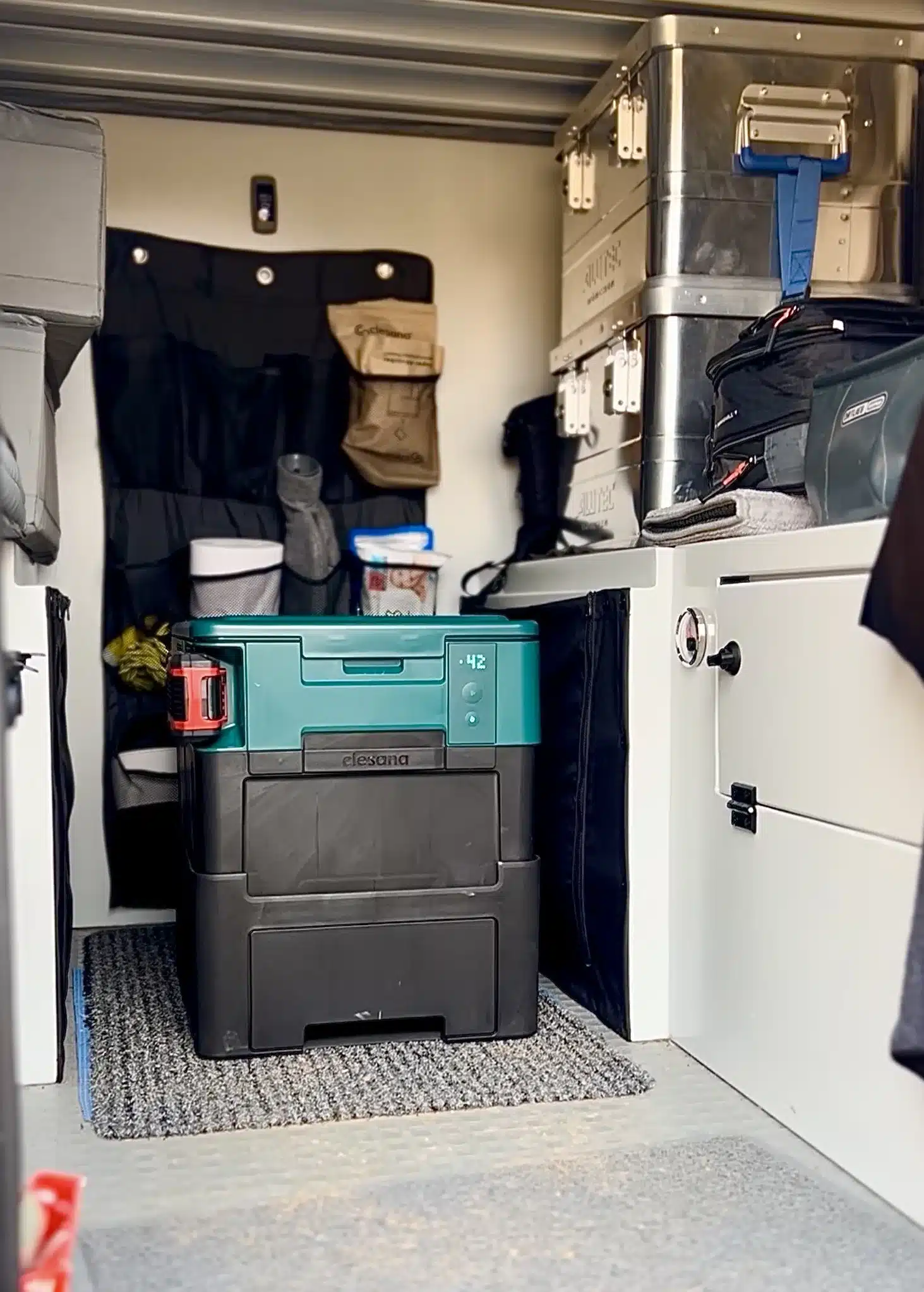 Clesana X1 Trenntoilette im Stauraum eines Campers, umgeben von Reiseausrüstung.