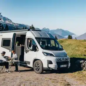 Kastenwagen Sunlight CLIFF Adventure mit Campingzubehör und zwei Personen in alpiner Landschaft
