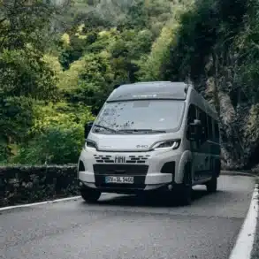 Frontansicht des Sunlight CLIFF X 640 Kastenwagens auf einer schmalen Straße zwischen Felsen und Bäumen