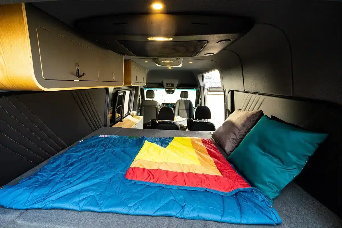 Blick in den ausgebauten Innenraum eines Campervans mit Querbett, Staufächern und Sitzen
