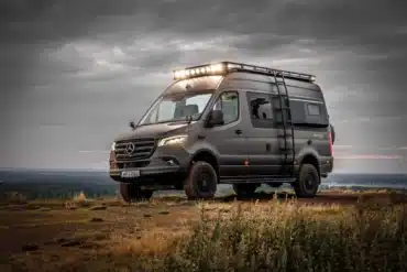 Grauer Dovra RIG X-610 4x4-Camper mit Dachträger, Leiter und LED-Licht auf unbefestigtem Gelände