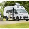 Dreamer Camper Sport Kastenwagen mit zwei Personen und Fahrrädern auf einem Stellplatz in grüner Umgebung.