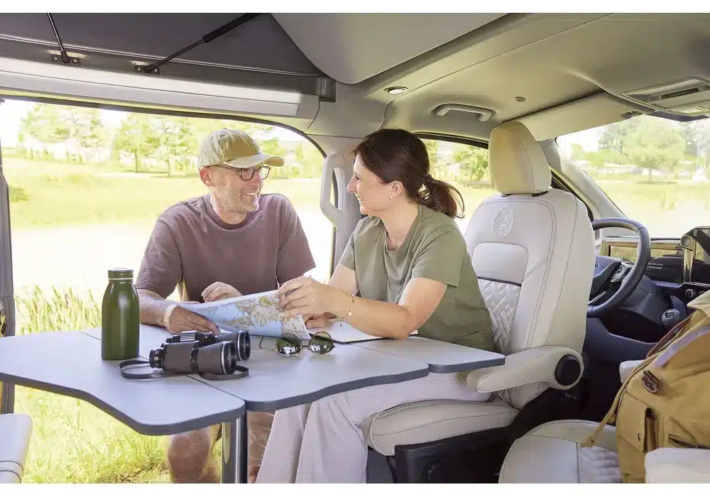 Zwei Menschen sitzen im Innenraum eines Dreamer Cap Land Campers an einem ausklappbaren Tisch und planen mit einer Karte ihre Reise.