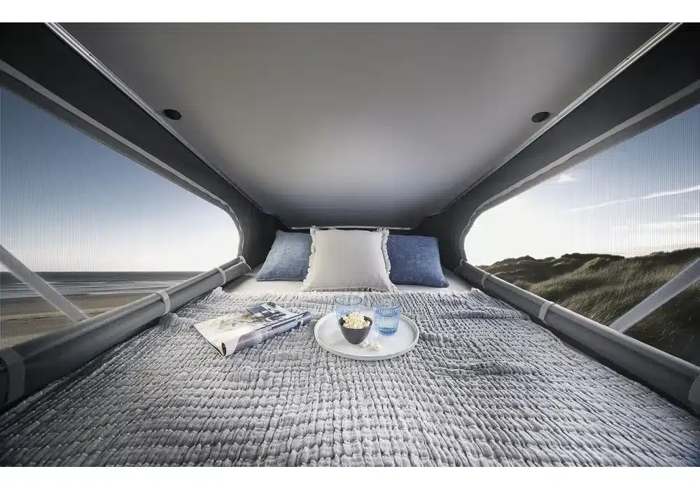 Blick ins Aufstelldach des Dreamer City Camp Select mit gemachtem Bett und Ausblick auf die Dünen.