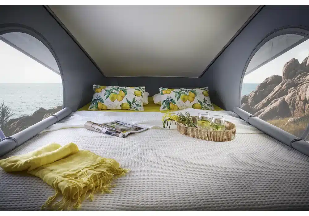 Aufstelldach-Bett im Dreamer D43 UP Select mit Kissen, Decke, Getränken und Panoramablick auf das Meer