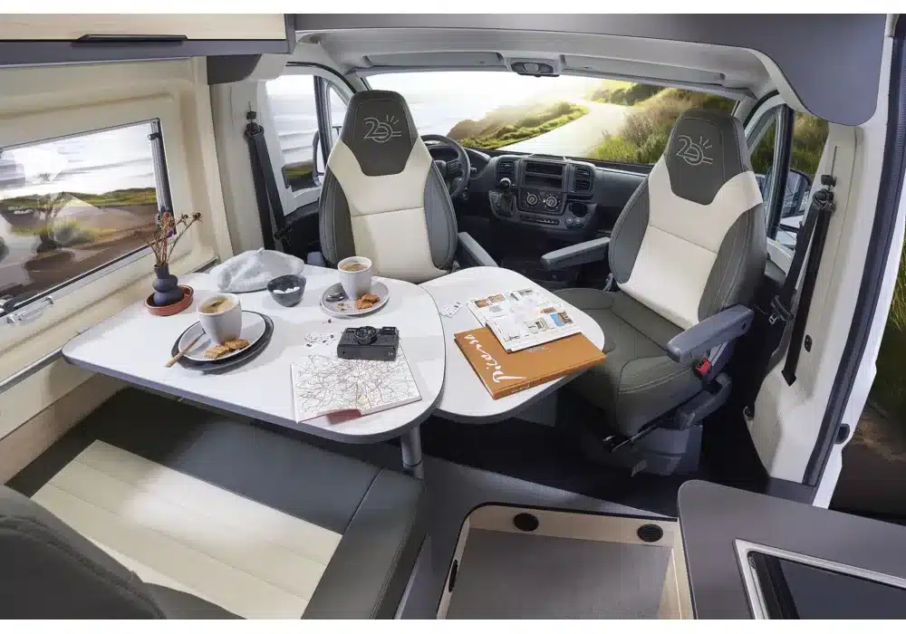 Wohn- und Essbereich im Dreamer D55 Kastenwagen mit gedecktem Tisch und drehbaren Fahrersitzen.