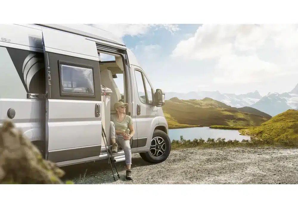 Dreamer D55 UP Kastenwagen mit geöffneter Seitentür, davor eine Person sitzend in alpiner Landschaft.