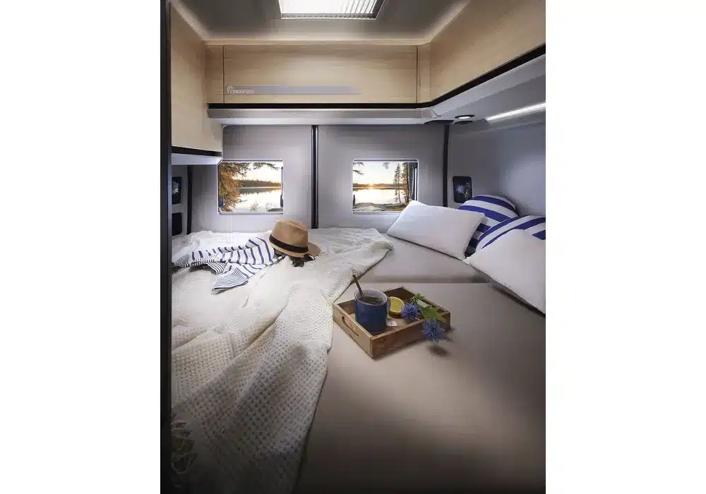 Festes Heckbett mit Kissen und Decken im Innenraum des Dreamer D55 Kastenwagens, mit Ausblick durch zwei Fenster.
