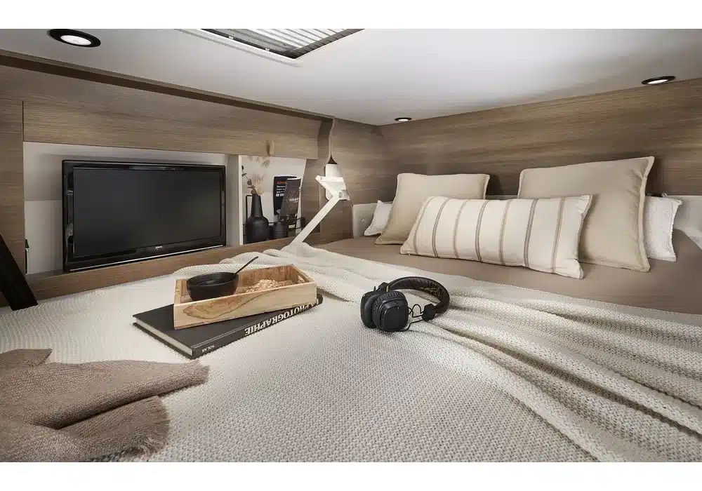 Innenansicht eines Hubbetts mit Kissen, TV und Ablage im Dreamer Family Van