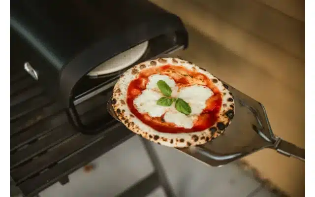 Frisch gebackene Pizza auf einer Pizzaschaufel vor dem Enders Paco Rotate Pizzaofen mit sichtbarem Pizzastein