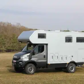 Iveco Daily 4x4 Achleitner mit Woelcke Wohnaufbau als Expeditionsmobil auf einer offenen Wiese vor Waldrand