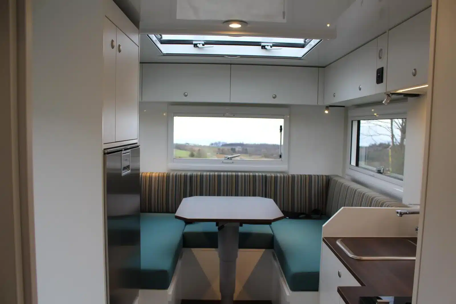 Innenansicht eines Wohnaufbaus mit Sitzgruppe, Tisch, Küchenzeile und großen Fenstern im Iveco Daily 4x4 Achleitner mit Woelcke Wohnaufbau.