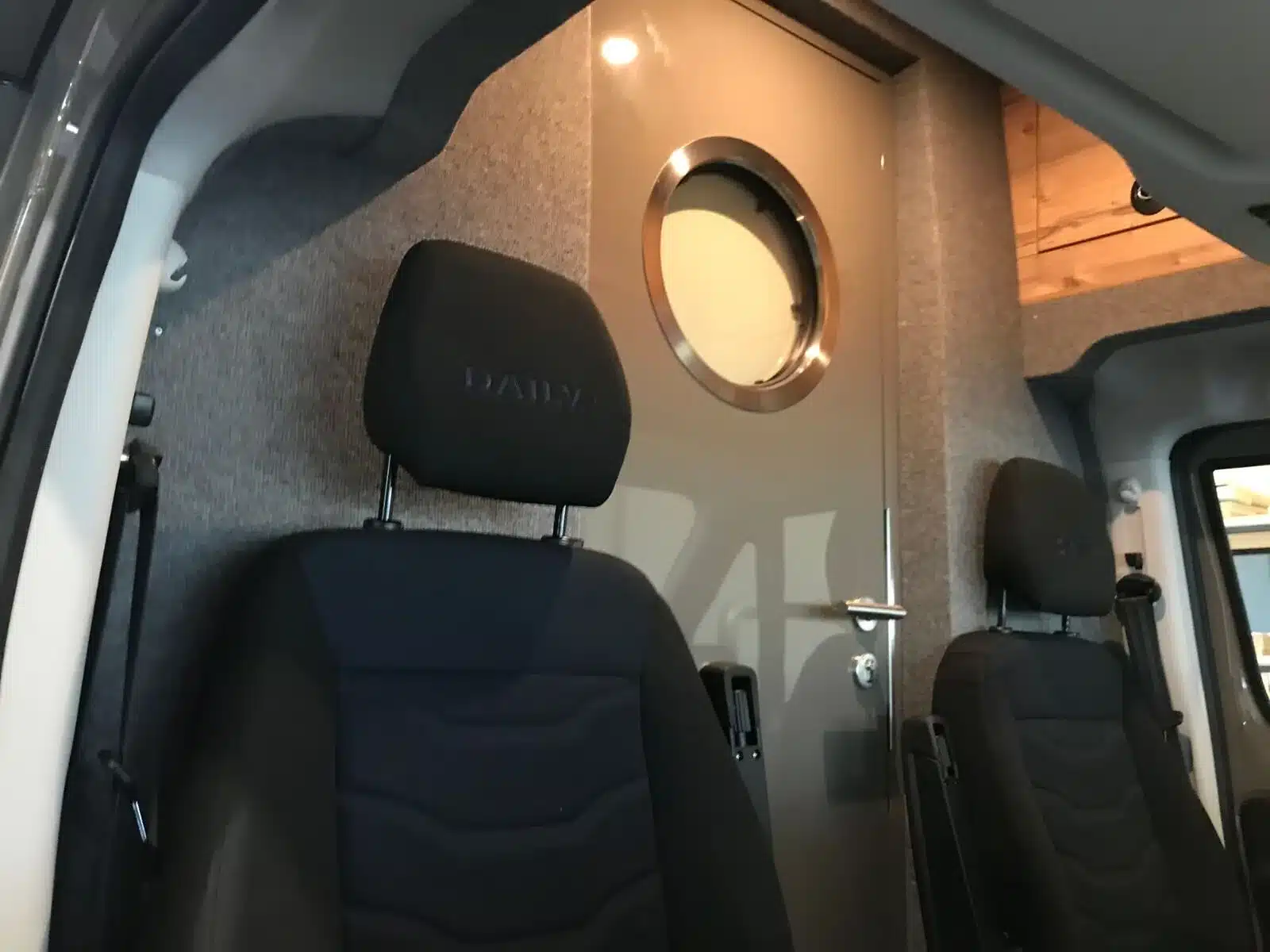 Fahrerkabine mit zwei Sitzen und grauer Trennwand samt runder Tür im Iveco Daily 4x4 Expeditionsmobil