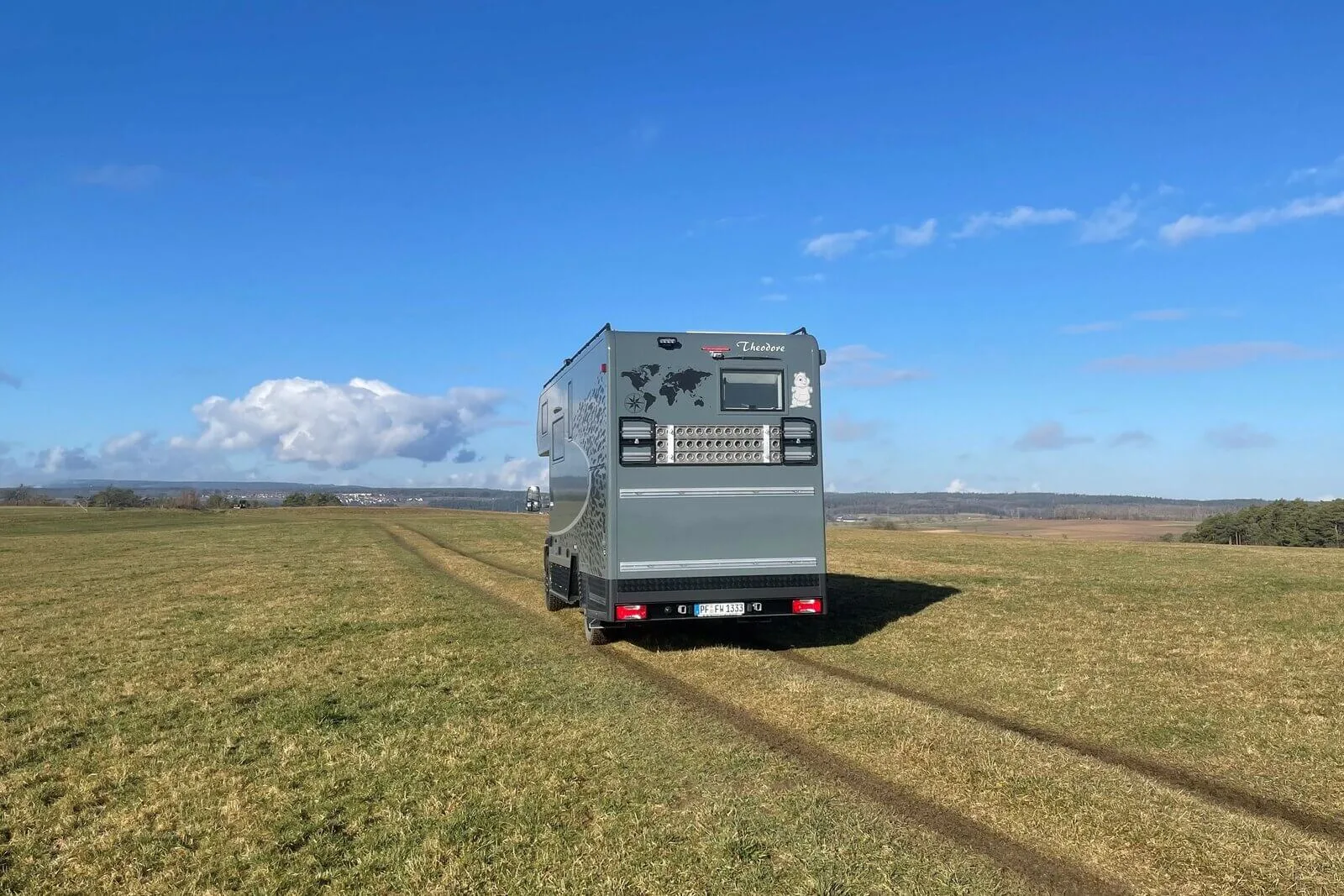 Reisemobil Woelcke Theodore auf Iveco Daily 4x4 Basis von hinten auf einer Wiese, Offroad-Spuren sichtbar.