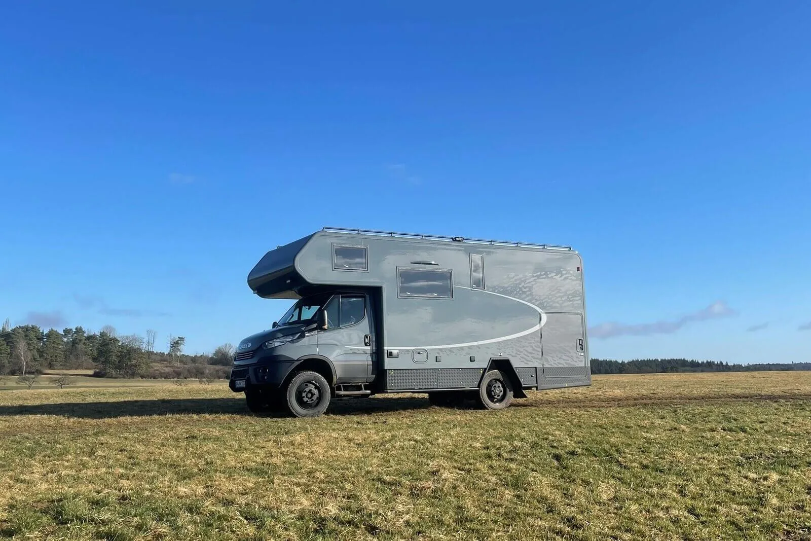 Seitenansicht eines Iveco Daily 4x4 Theodore Reisemobil mit Woelcke Wohnaufbau, stehend auf einer Wiese unter blauem Himmel