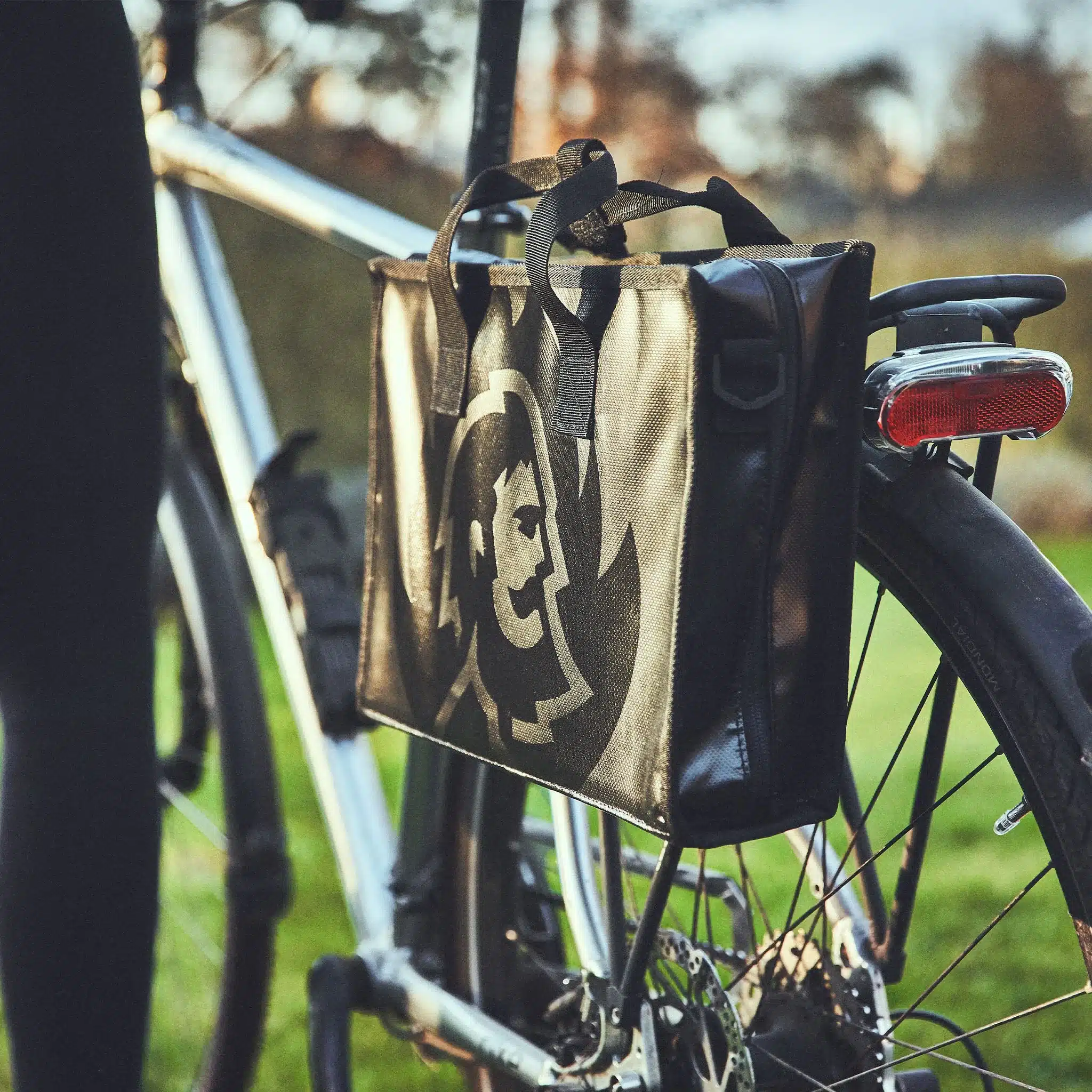 Tragetasche des JONES Jr. Campinggrills am Fahrradträger befestigt, Symbol für flexible Mobilität beim Camping.