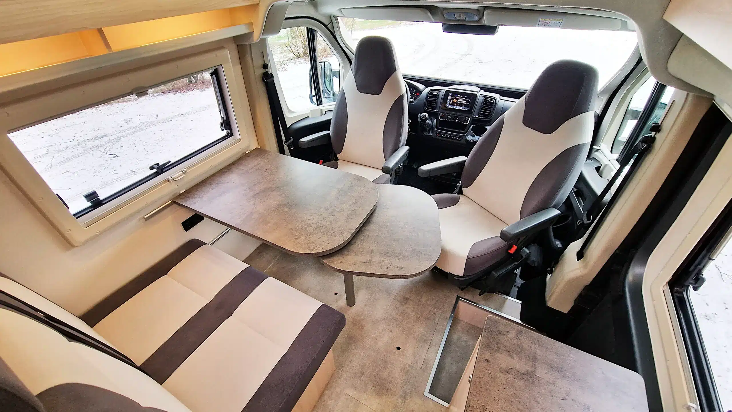 Innenansicht der Sitzgruppe und Fahrerhaussitze im BRESLER JUNIOR 541 DK Reisemobil mit Tisch und hellen Polstern.