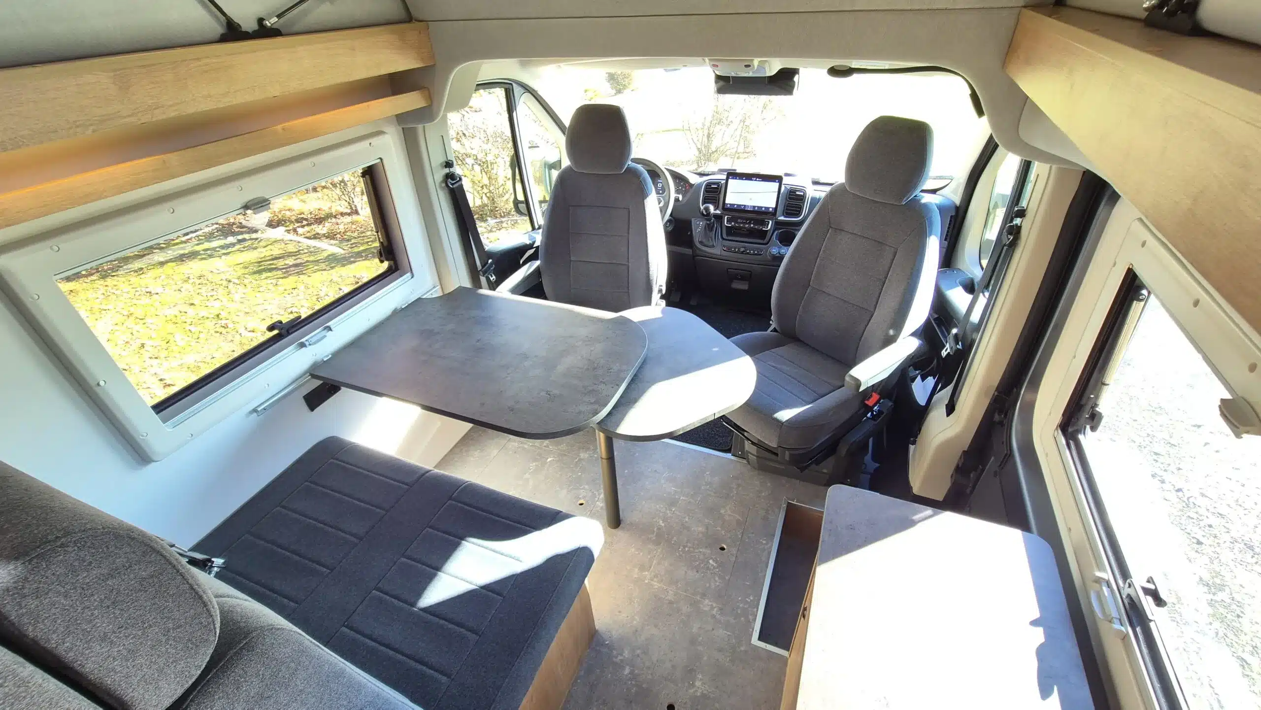 Sitzbereich und Fahrerhaus im kompakten Reisemobil Bresler Junior 541 DK mit Esstisch und großen Fenstern