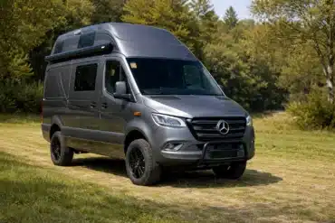 BRESLER Junior Exclusiv Campervan auf Mercedes Sprinter Basis mit Hochdach, abgestellt auf einer Wiese vor Waldkulisse.