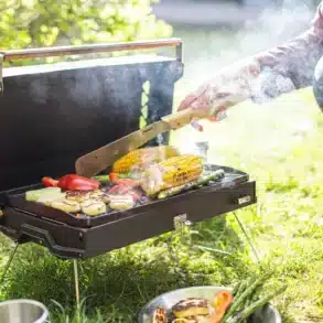 Offener Kuchoma Portable Grill mit gegrilltem Gemüse und Maiskolben auf einer Wiese.