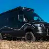 Schwarzer Mercedes-Benz Sprinter L3H2 Campervan La Onda mit Wellenmuster auf einem Feld unter blauem Himmel