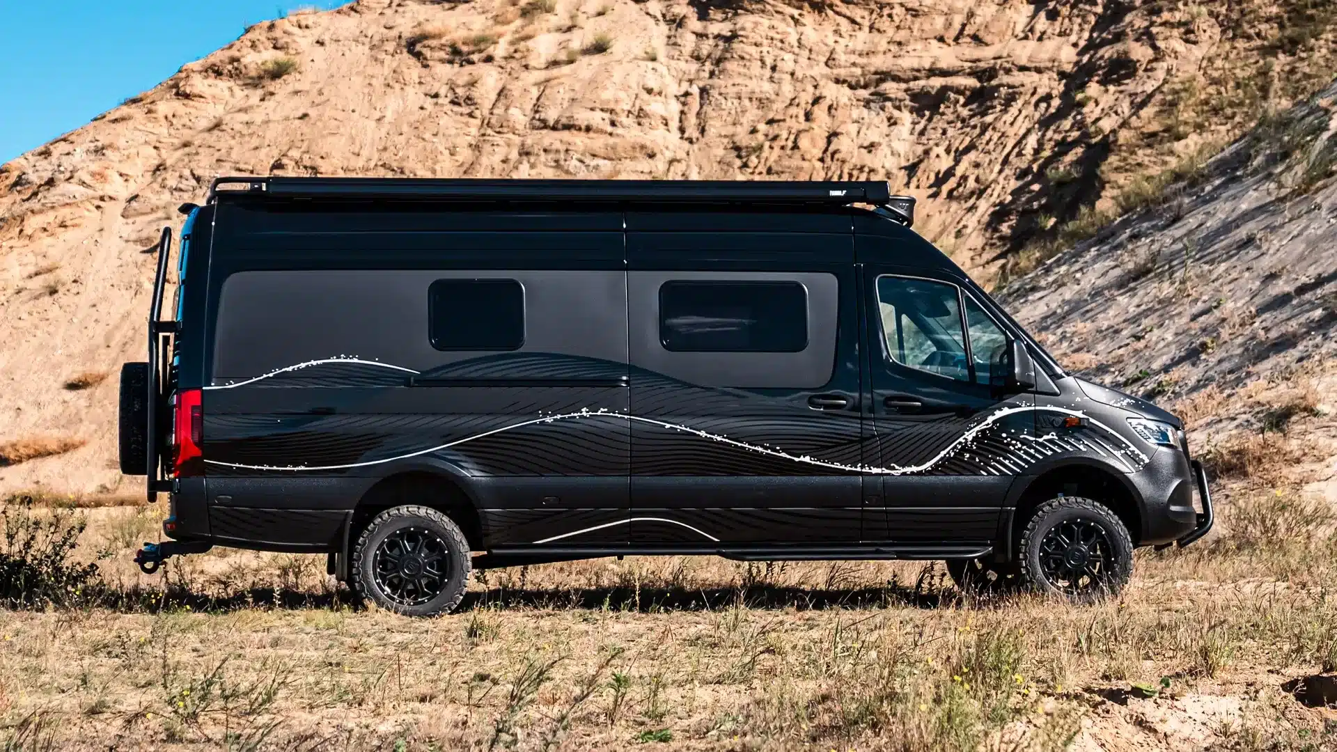 Schwarzer Mercedes-Benz Sprinter La Onda Campervan mit auffälligem Wellenmotiv und Offroad-Ausstattung in der Seitenansicht.