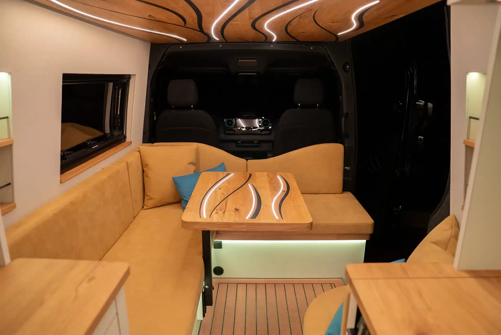 Wohnbereich im La Onda Campervan mit charakteristischer Echtholzdecke, LED-Licht in Wellenform und Designtisch.