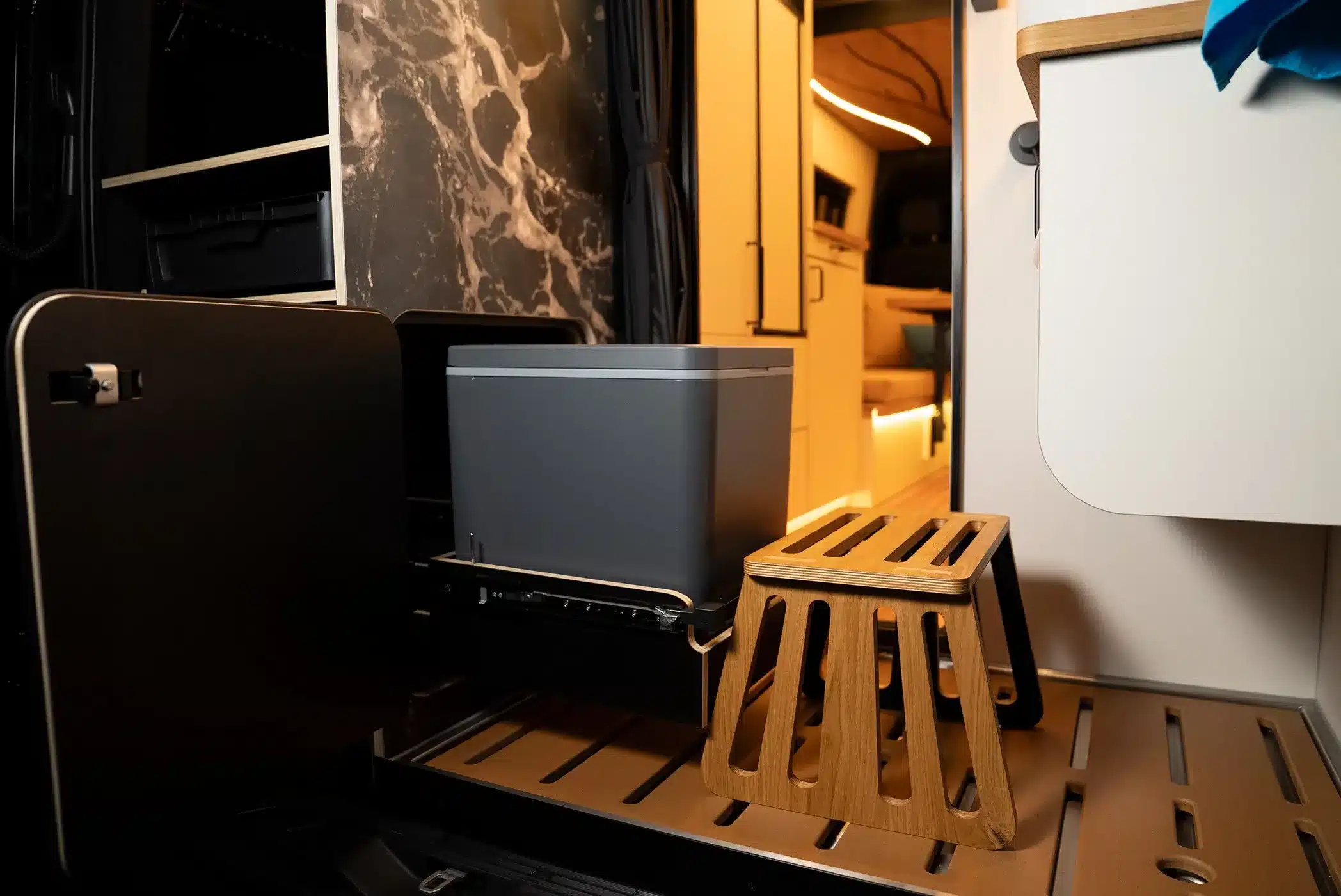 Ausziehbare Kühlbox und Holztritt im Heck des La Onda Campervans, mit Blick auf den hochwertigen Innenraum und stimmungsvolle Beleuchtung.