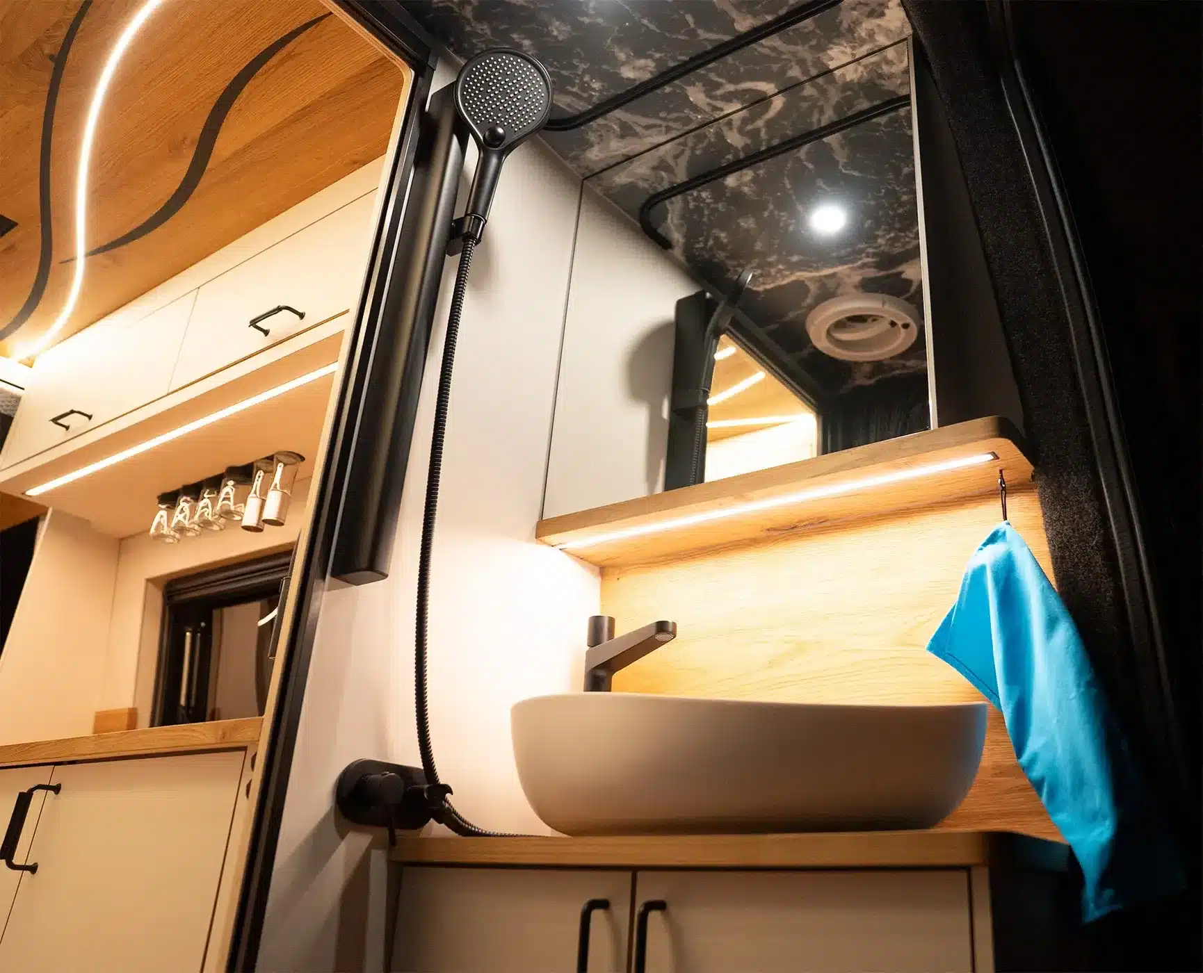 Innenansicht des La Onda Campervans: Modernes Bad mit Waschbecken, Duschkopf, Wellenmuster-Decke und angrenzender Küche.