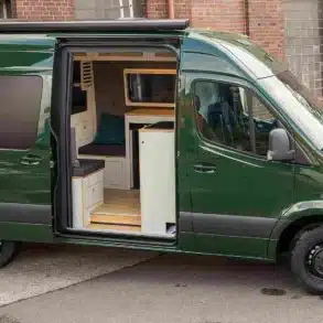 Der ausgebaute grüne Mercedes-Benz Sprinter Campervan Libelle mit geöffneter Schiebetür und Blick auf den wohnlichen Innenraum.